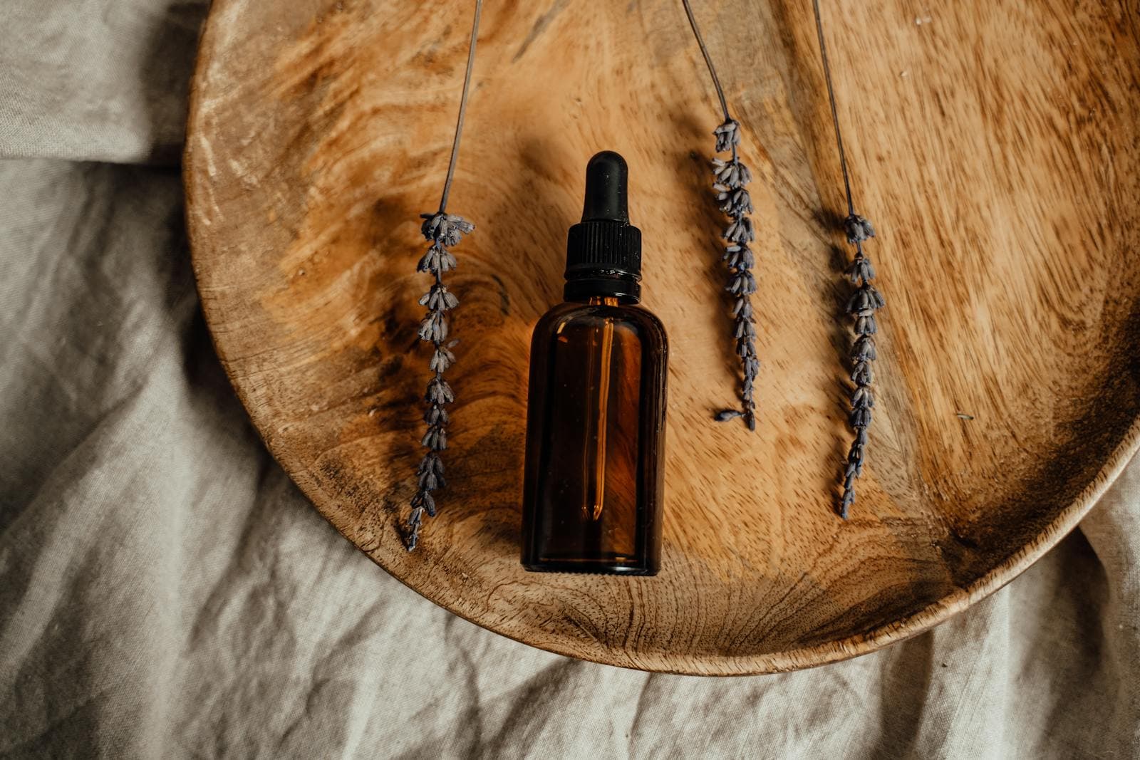 An amber dropper bottle and dried lavender on a wooden dish, in natural light